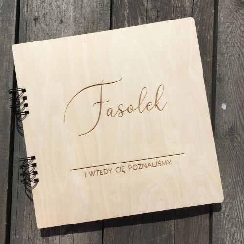 Drewniany album na zdjęcia z sesji ciążowej z grawerem "Fasolek" i tekstem "I wtedy Cię poznaliśmy" na okładce.