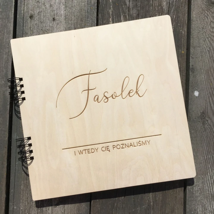 Drewniany album na zdjęcia z sesji ciążowej z grawerem "Fasolek" i tekstem "I wtedy Cię poznaliśmy" na okładce.