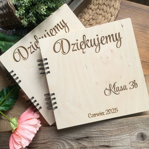 Personalizowany album dla nauczyciela leżący na wiklinowej podkładce obok ozdobnych traw.