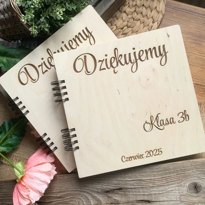 Personalizowany album dla nauczyciela leżący na wiklinowej podkładce obok ozdobnych traw.
