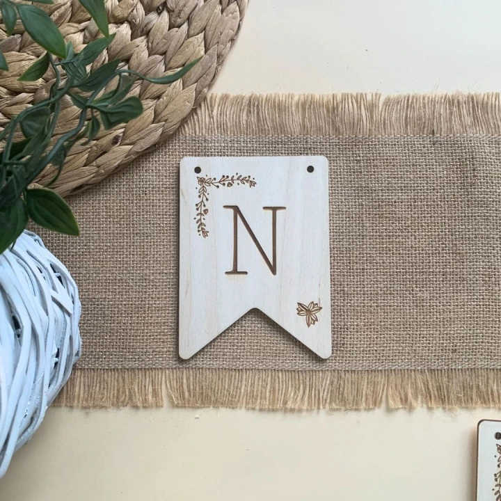 Zbliżenie na grawerowaną literę N z botanicznym wzorem, element personalizowanej drewnianej girlandy do pokoju dziecka.