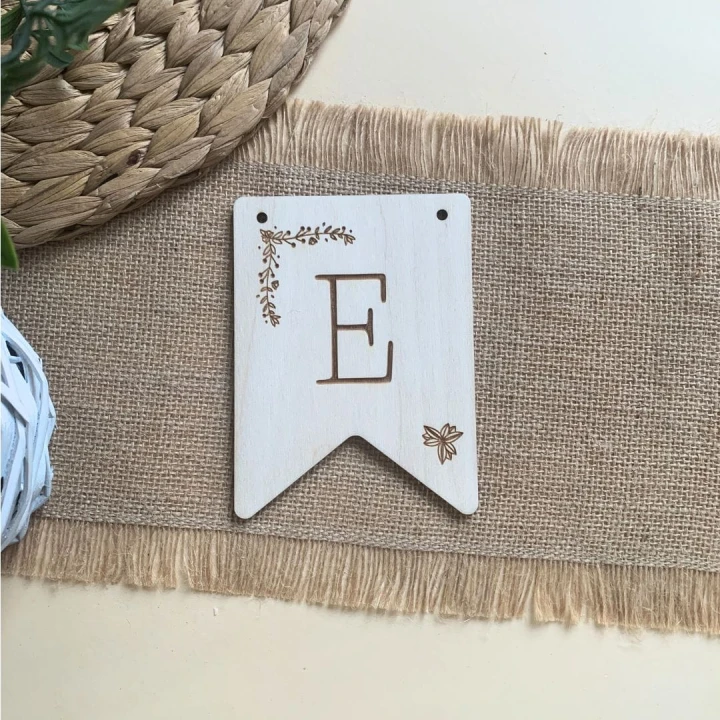 Tabliczka ze sklejki, grawer z literą E i delikatnym roślinnym detalem, element girlandy.