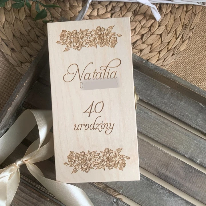 Drewniane pudełko na pieniądze z personalizowanym grawerem imienia i wieku, ze wstążką.
