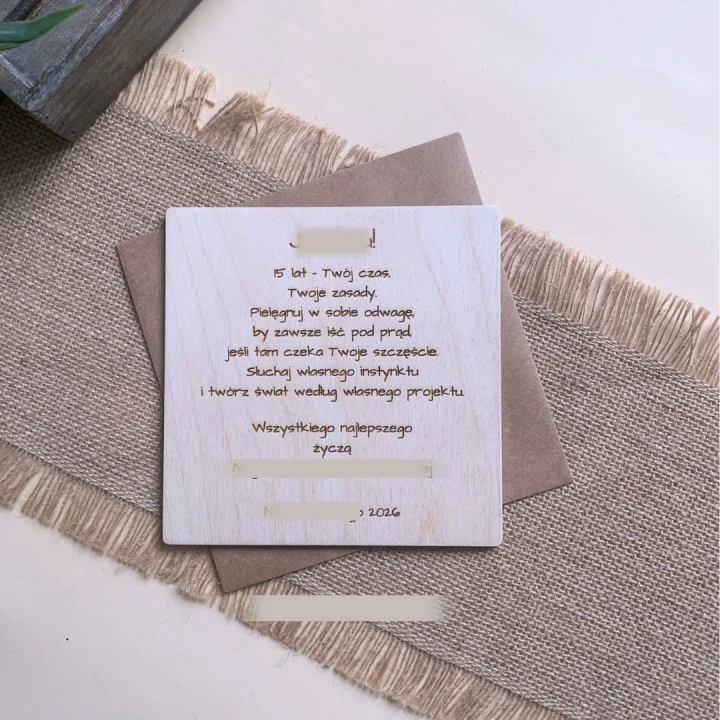 Rewers drewnianej kartki z wygrawerowanymi personalizowanymi życzeniami urodzinowymi na jasnej sklejce.
