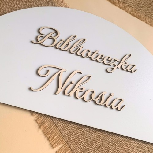 Biała tablica HDF w kształcie półkola z naklejonym drewnianym napisem Biblioteczka z imieniem.