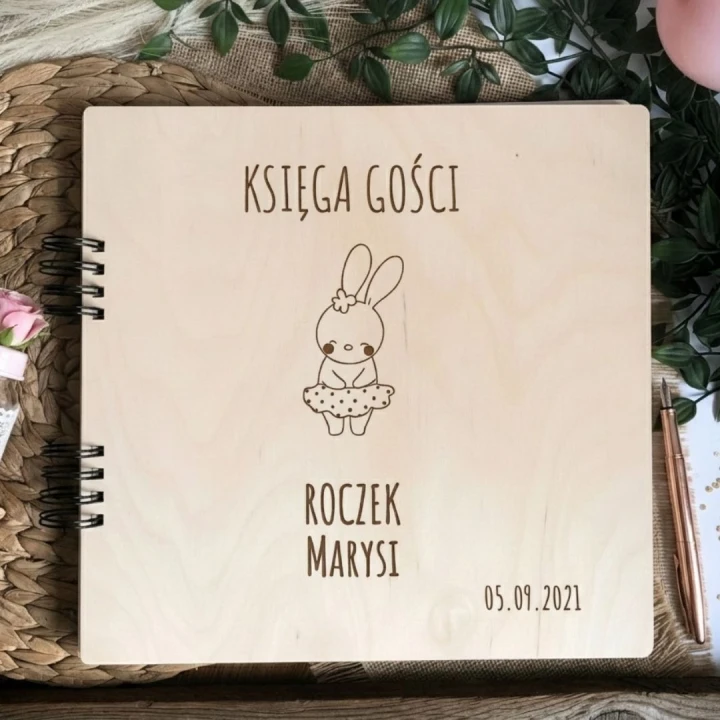 Drewniana księga gości na pierwsze urodziny w aranżacji boho z różowymi dodatkami i eleganckim długopisem.