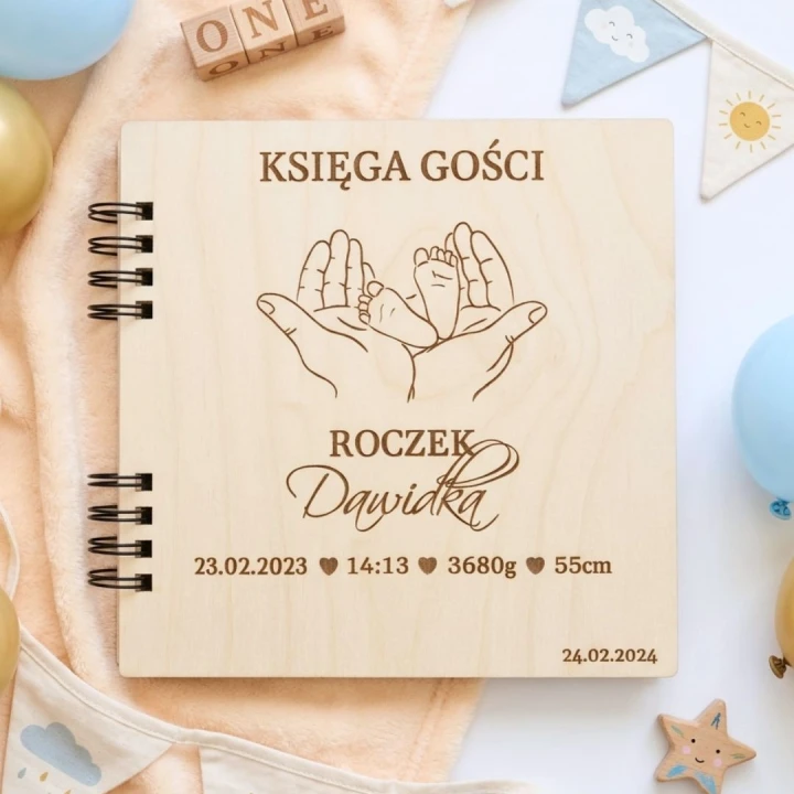 Drewniana księga gości na roczek z grawerem stópek niemowlęcia w dłoniach rodziców.