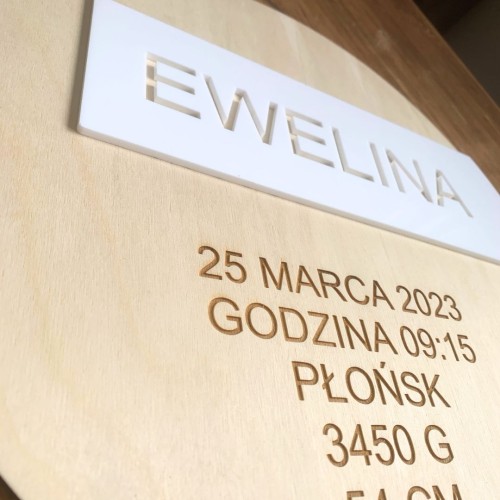 Okrągła drewniana metryczka urodzenia dla dziecka . Zbliżenie na imię wycięte w prostokątnej, białej plexi (efekt 3D)