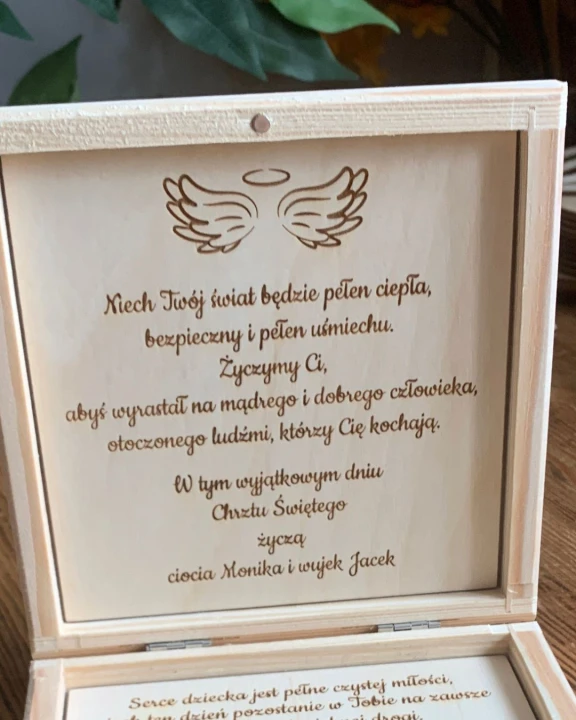 Otwarte drewniane pudełko Pamiątka Chrztu Kacperka. We wnętrzu wieka widoczny ozdobny tekst personalizowanych życzeń z motywem skrzydełek aniołka.